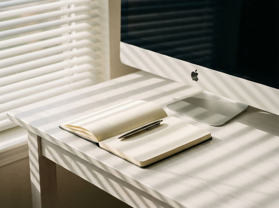 A bright airy studio with white walls, large windows, a glass desk with a slim laptop