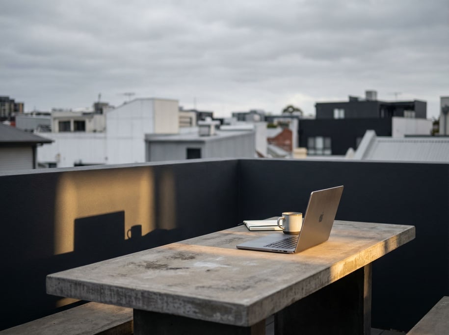 A rooftop workspace setup, laptop on a simple outdoor table, overcast sky, blurred city behind (g4omoduz)