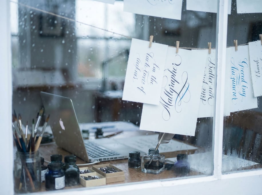 A calligrapher's workspace, laptop next to ink bottles, nibs (fk6hsiwz)